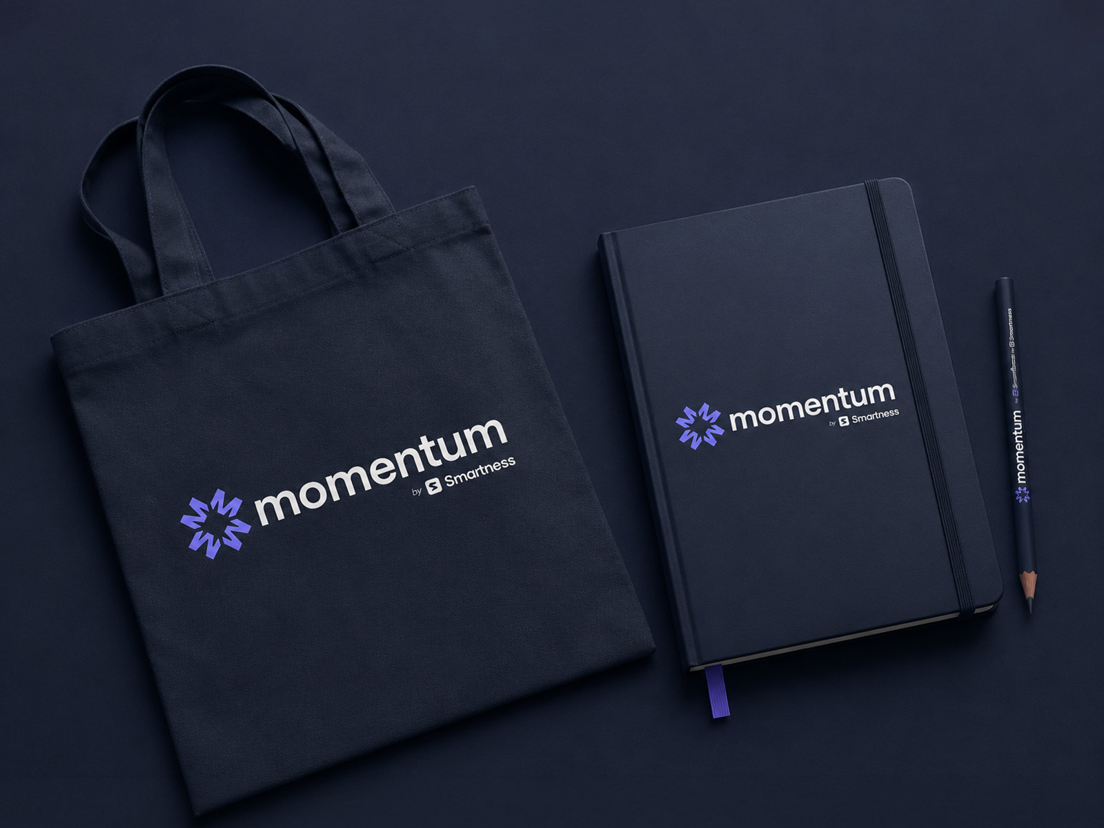 A navy Momentum tote bag, a matching hardback notebook and a pencil, each carrying the logo in purple and white on a dark background.